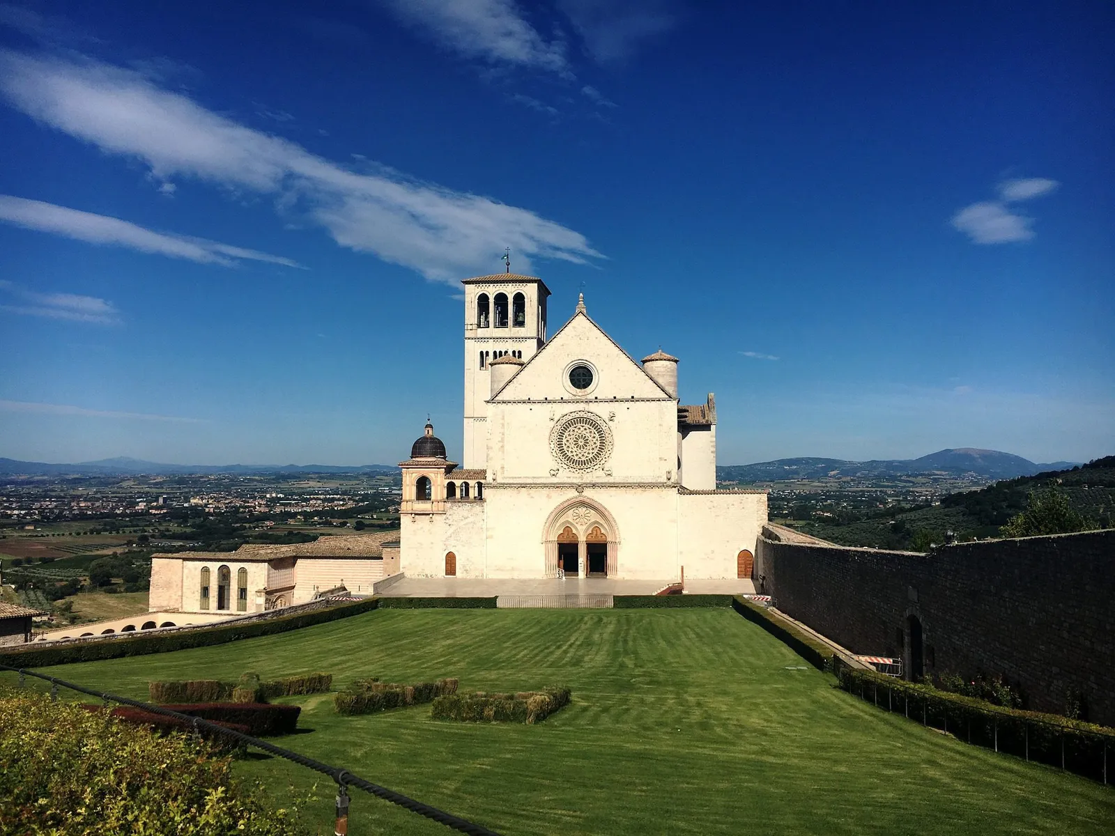 La basilica di San Francesco ad Assisi con il prato in pendenza e la valle