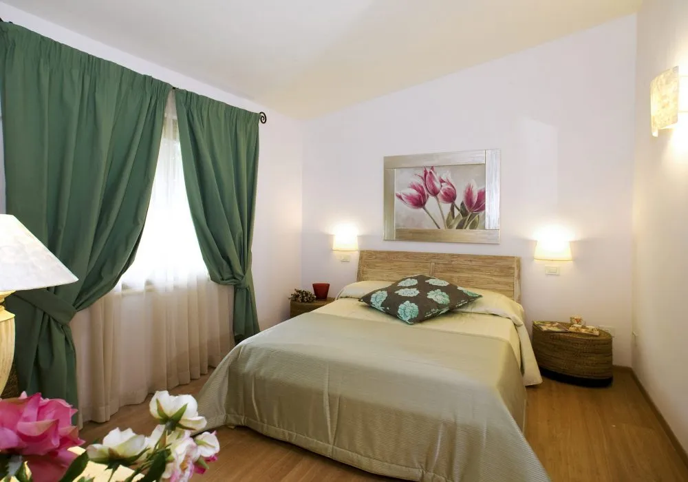 Camera con tende verdi, testata in legno chiaro e quadro di tulipani rosa
