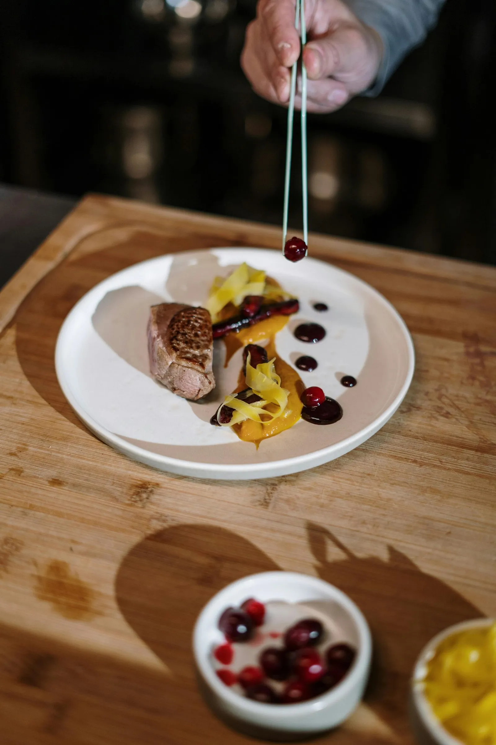 Mano dello chef che posa un mirtillo rosso con una pinza su un piatto di carne