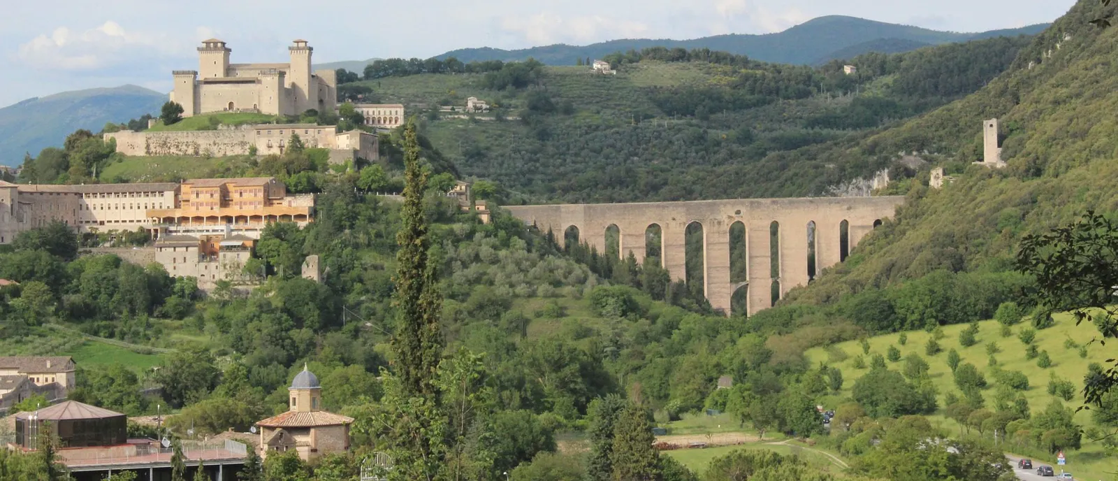 Panorama di Spoleto con la rocca sul colle e il ponte ad arcate fra i boschi